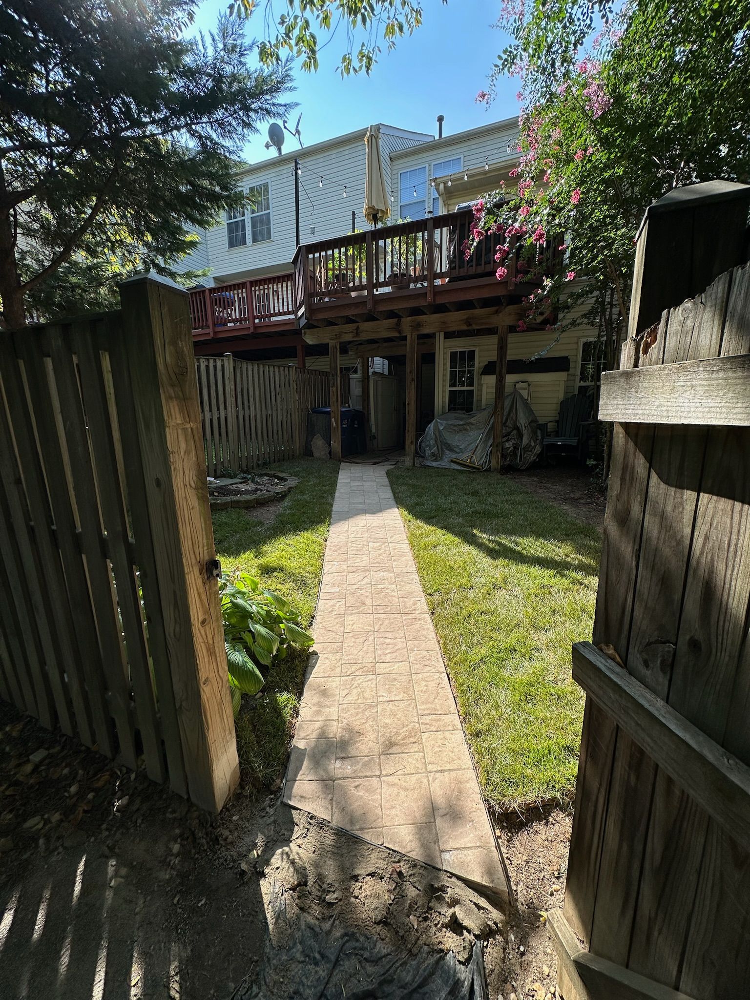 A path leading to a house with a deck and a wooden fence.