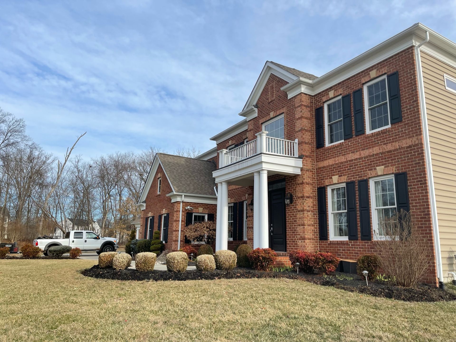 A large brick house with black shutters is sitting on top of a lush green lawn.