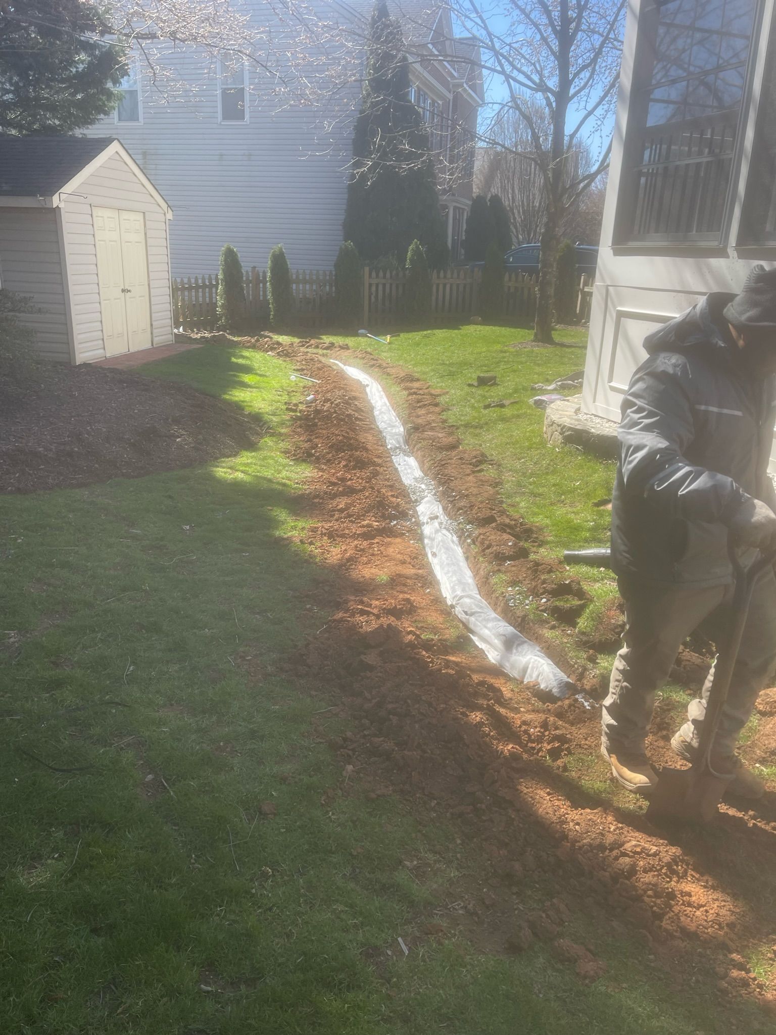 A man is working on a drain in a backyard.