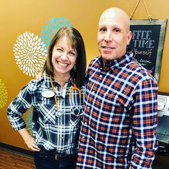 A man and a woman are posing for a picture in front of a sign that says coffee time yourself