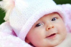 A baby wearing a pink hat is laying on a pink blanket.