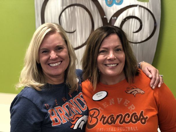 Two women wearing broncos shirts are posing for a picture