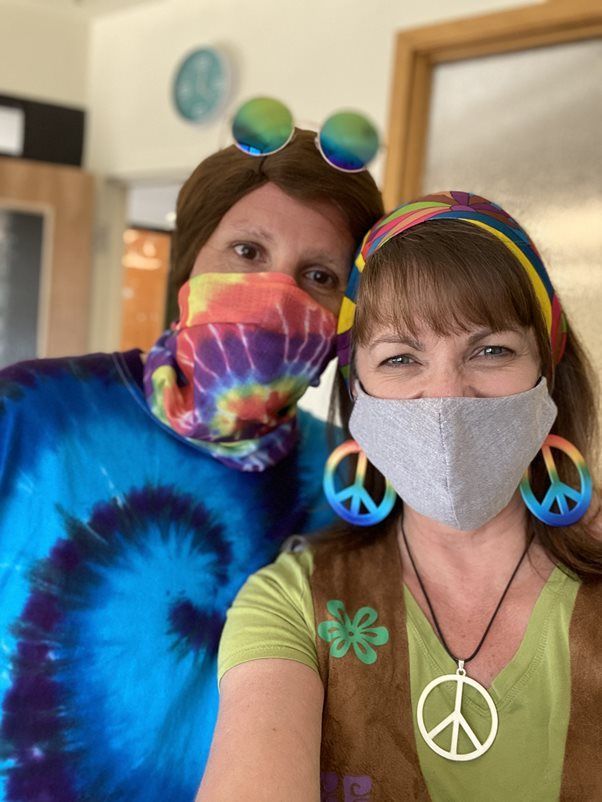A man and a woman wearing face masks and tie dye shirts are posing for a picture.