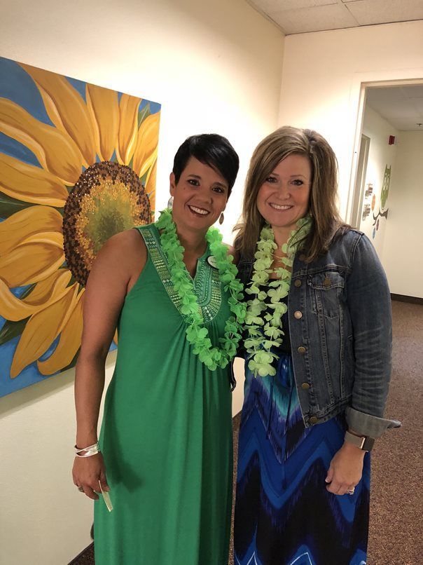 Two women are posing for a picture in front of a painting of a sunflower