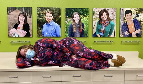 A woman wearing a mask is laying on a counter in front of a wall of pictures.
