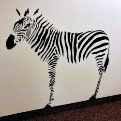 A black and white zebra is standing on a white wall.