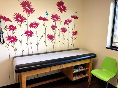 A pediatrician's office with a table and chairs and flowers on the wall