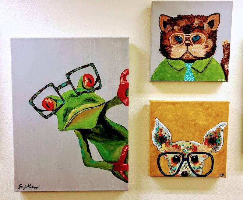 Three paintings on a wall one of which is of a frog wearing glasses