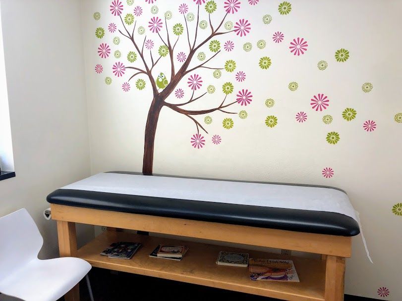 A pediatrician's office with a table and chairs and a tree on the wall