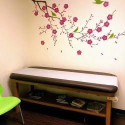 A pediatrician's office with a bench and a chair and a cherry blossom wall decal.