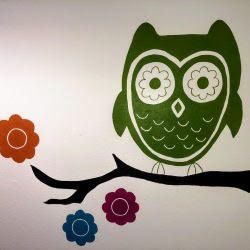 A green owl is sitting on a branch with flowers.