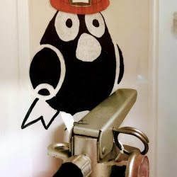 A black bird wearing a red hat is sitting on top of a fire extinguisher.