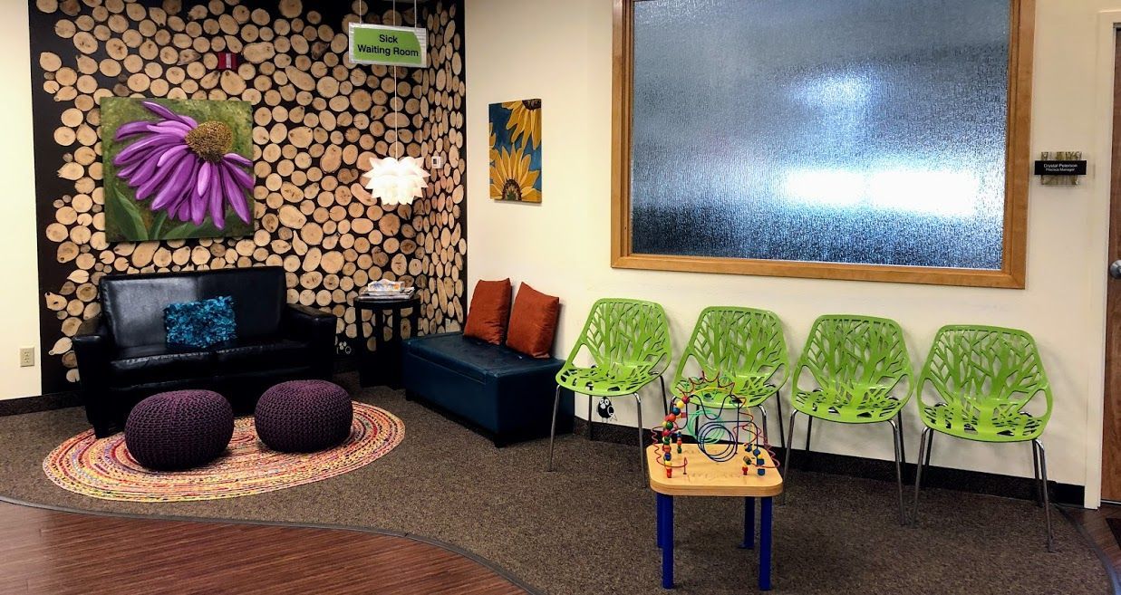 A waiting room with a couch , chairs , ottomans and a table.