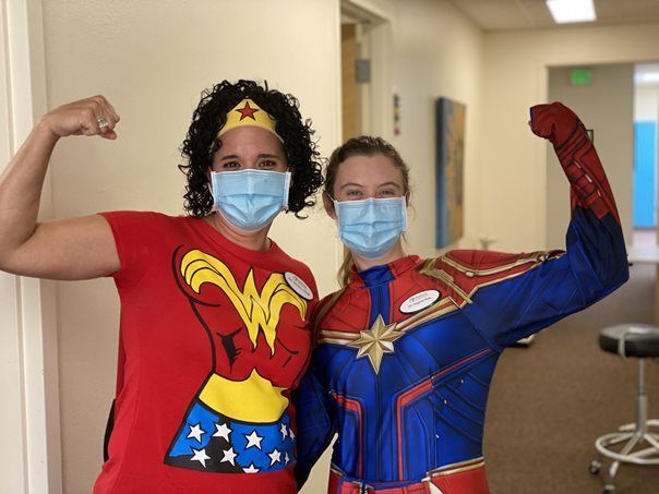 A woman in a wonder woman shirt and a woman in a captain marvel costume are posing for a picture.
