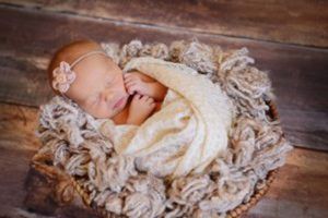 A newborn baby is sleeping in a basket on a wooden floor.