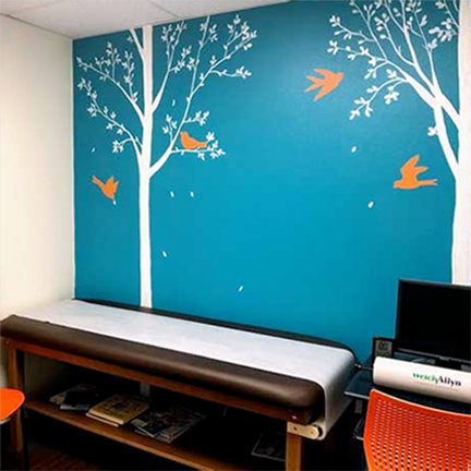 A pediatrician's office with trees and birds painted on the wall