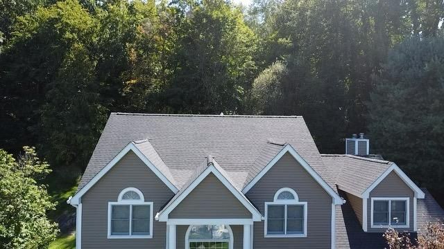 Gray house with dark roof, white trim, arched windows, and lush green trees in background.