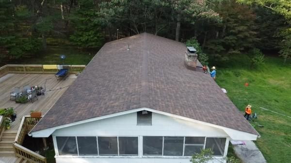A house with a brown shingled roof and a white screened-in porch. A deck and trees are visible.