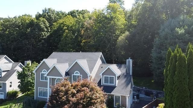 House with gray siding, dark roof, and chimney, surrounded by green trees and lawn.