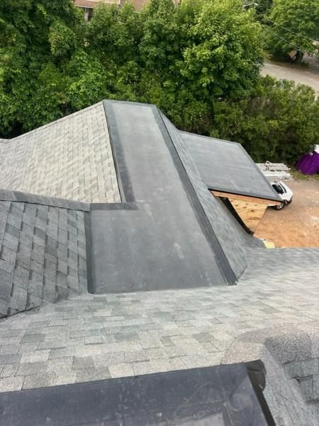 Gray shingle roof with dark gray flashing. Construction setting with trees in the background.