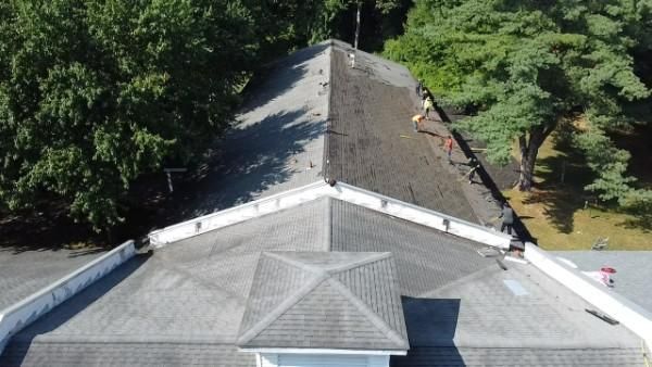 Aerial view of a house roof with one side being worked on, surrounded by trees.
