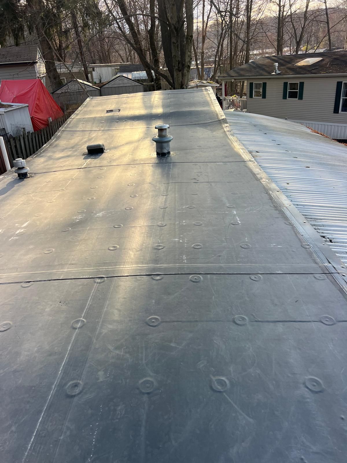 Dark flat roof with circular fasteners, vent, and light reflections; snow and houses in the background.