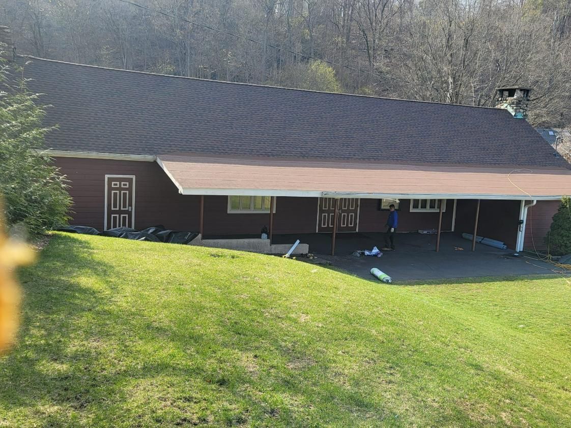 Red building with dark roof, covered porch, surrounded by green grass, trees in the background.