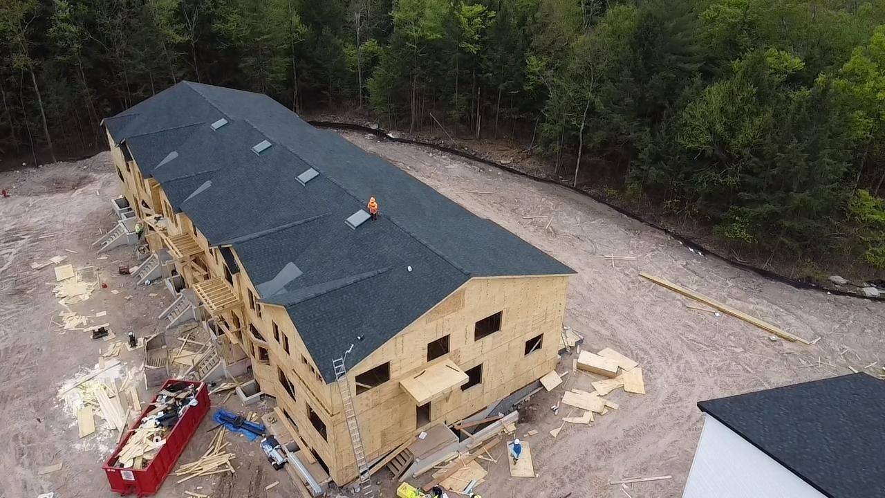 Construction of a wooden building with a black roof. A worker is visible on the roof.