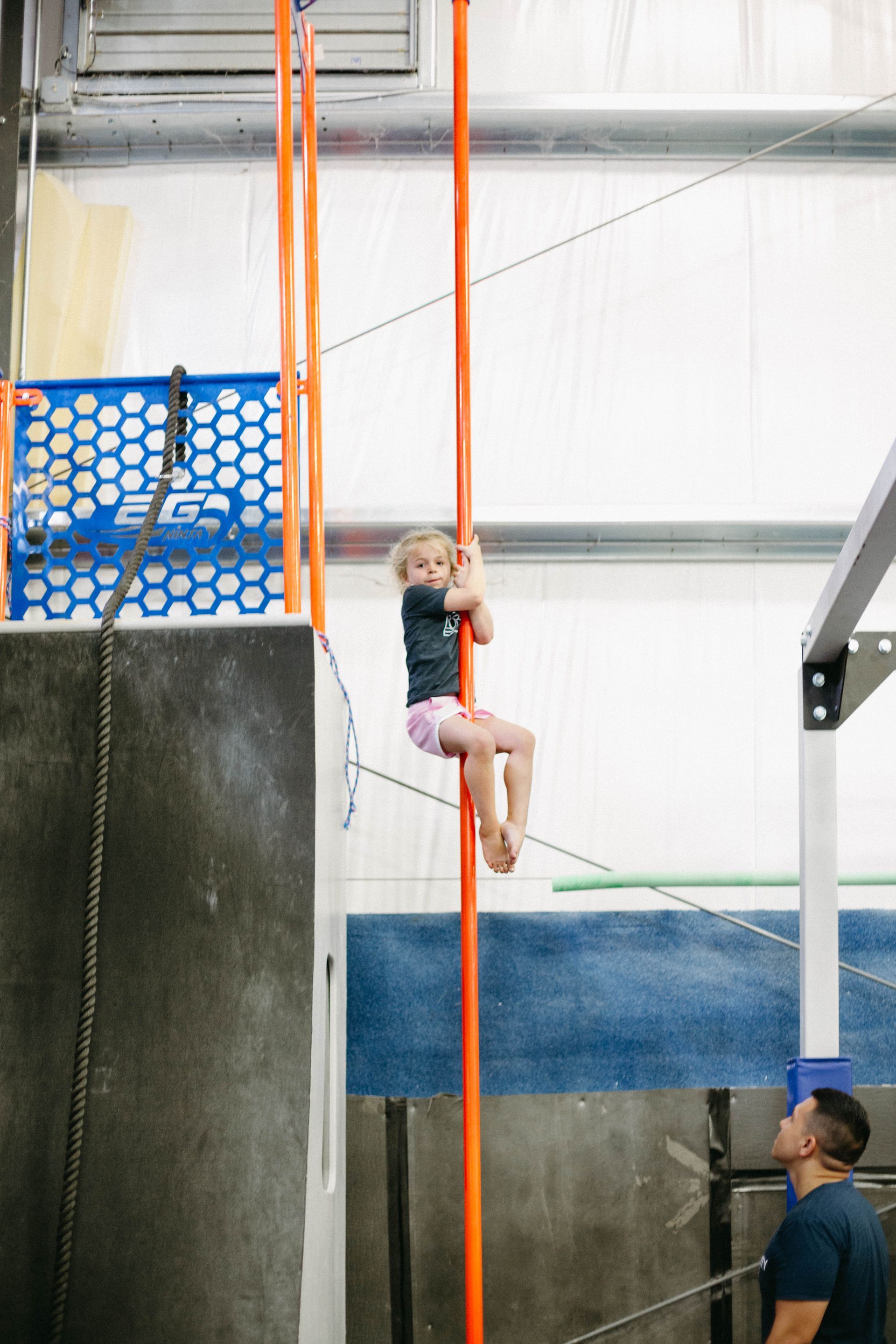 A little girl is climbing a pole in a gym.