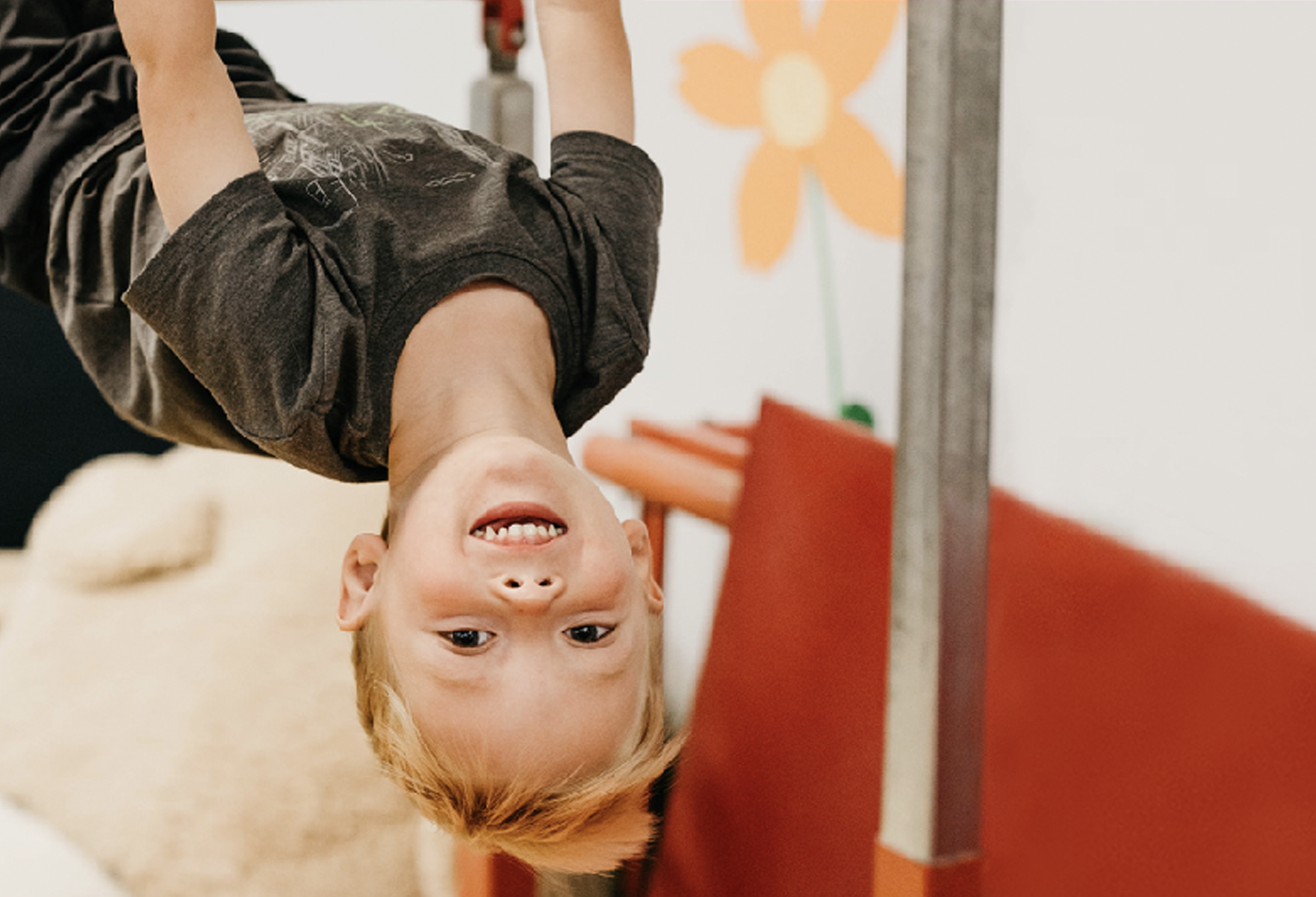 A young boy is hanging upside down from a pole.