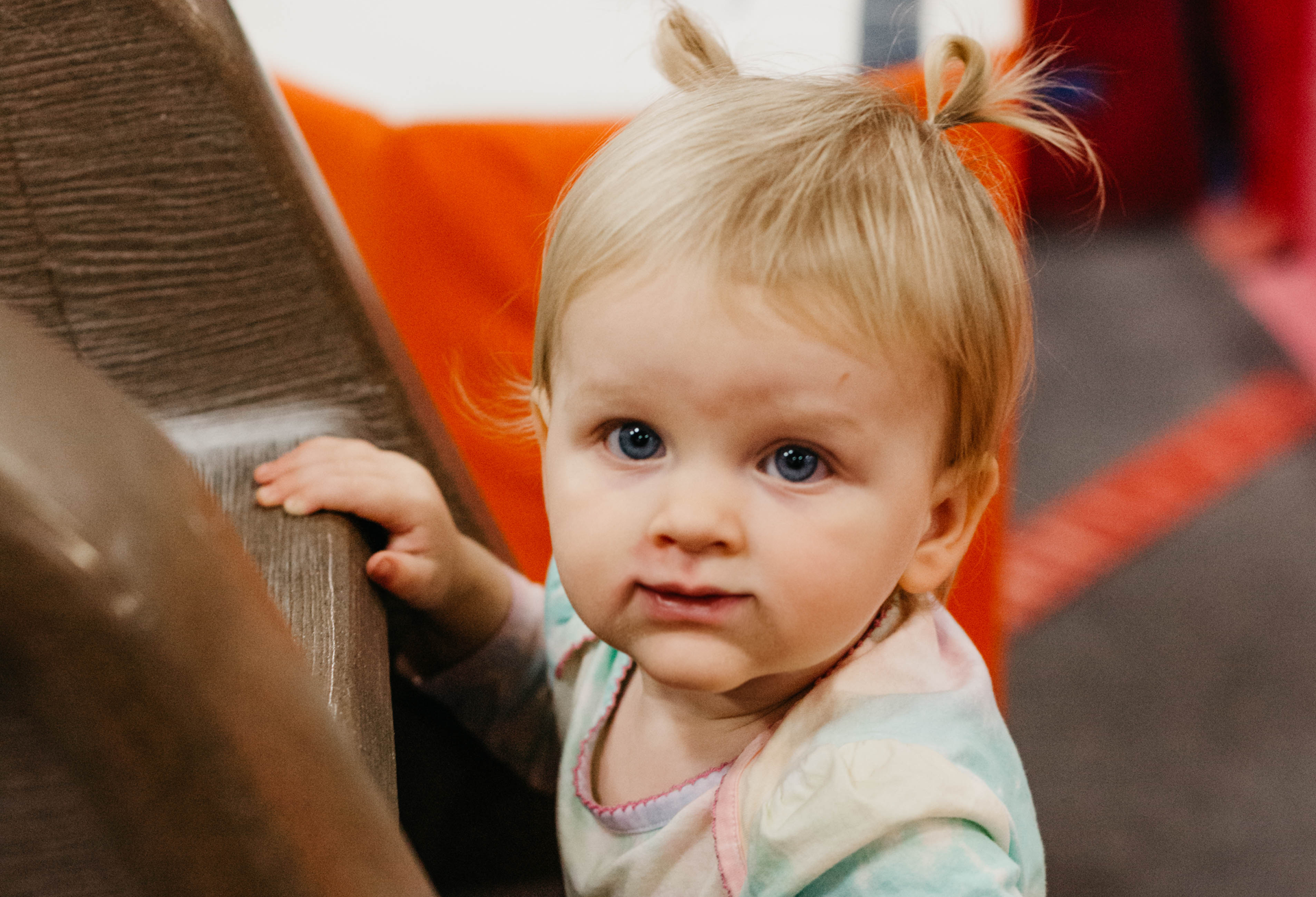 A baby girl is standing on a slide and looking at the camera.