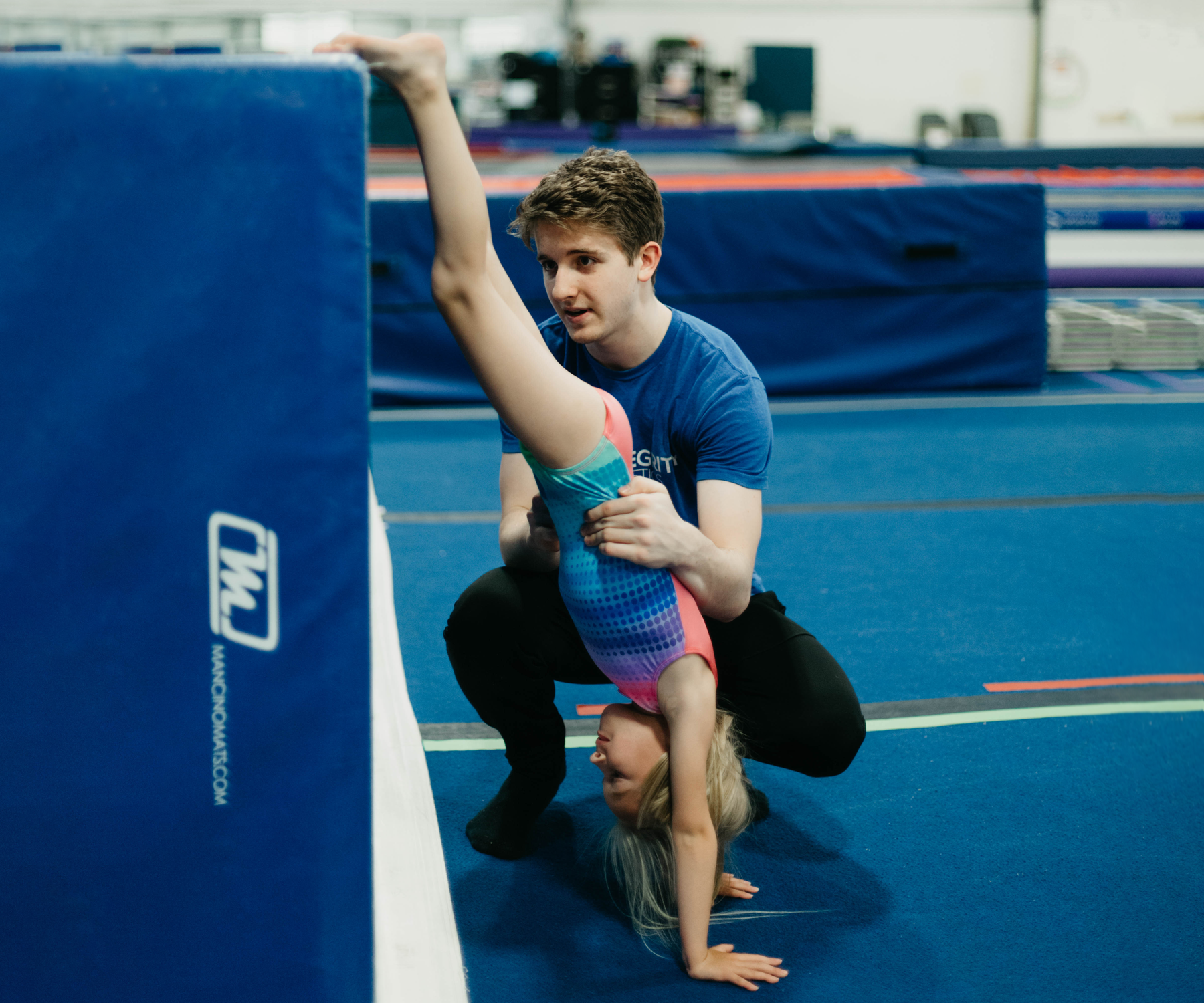 A man is helping a little girl do a handstand on the floor