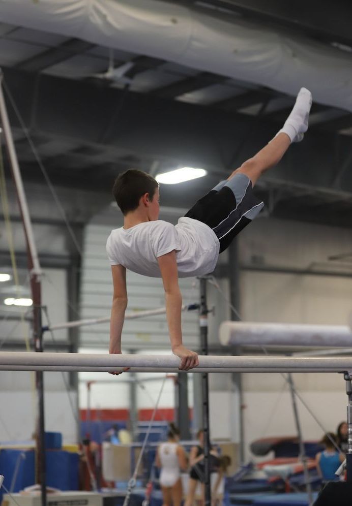 A young boy is doing a handstand on a parallel bars in a gym.