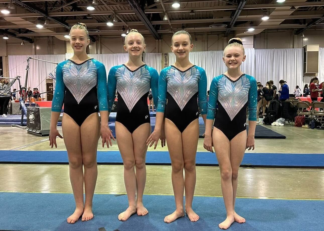 A group of young girls are standing next to each other on a gymnastics mat.