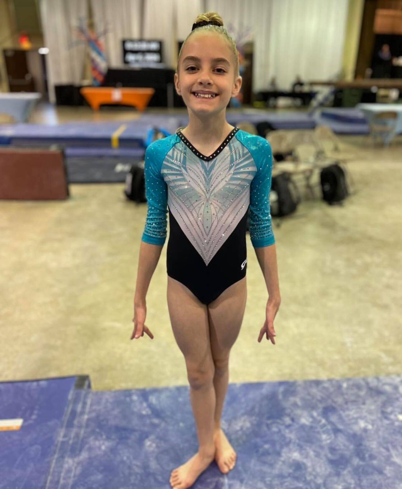 A young girl in a blue and black leotard is standing on a blue mat.