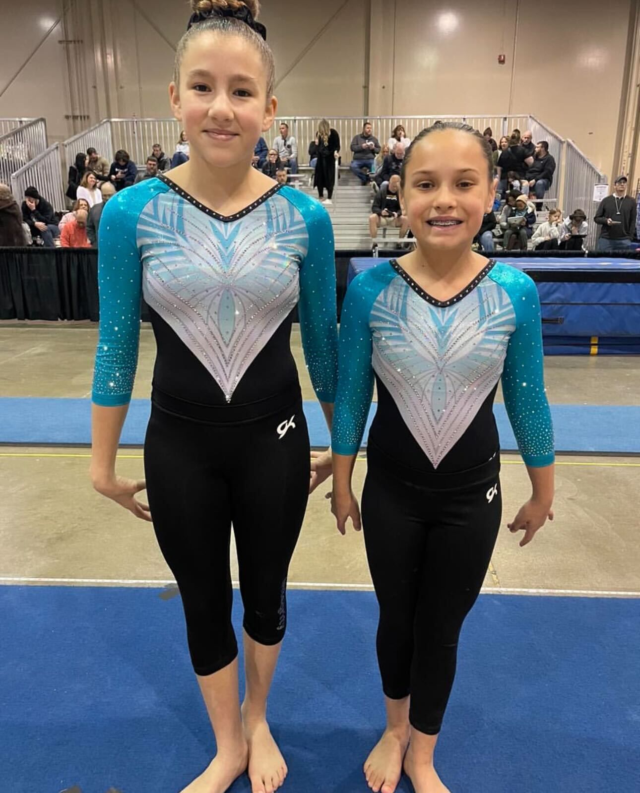 Two young girls are standing next to each other on a gym floor