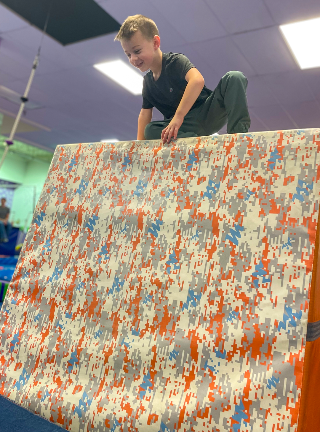 A young boy is standing on top of a camouflage mat.