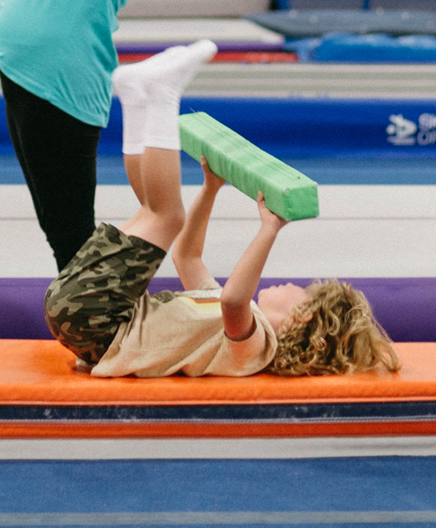 A child is laying on a bench holding a green foam bar