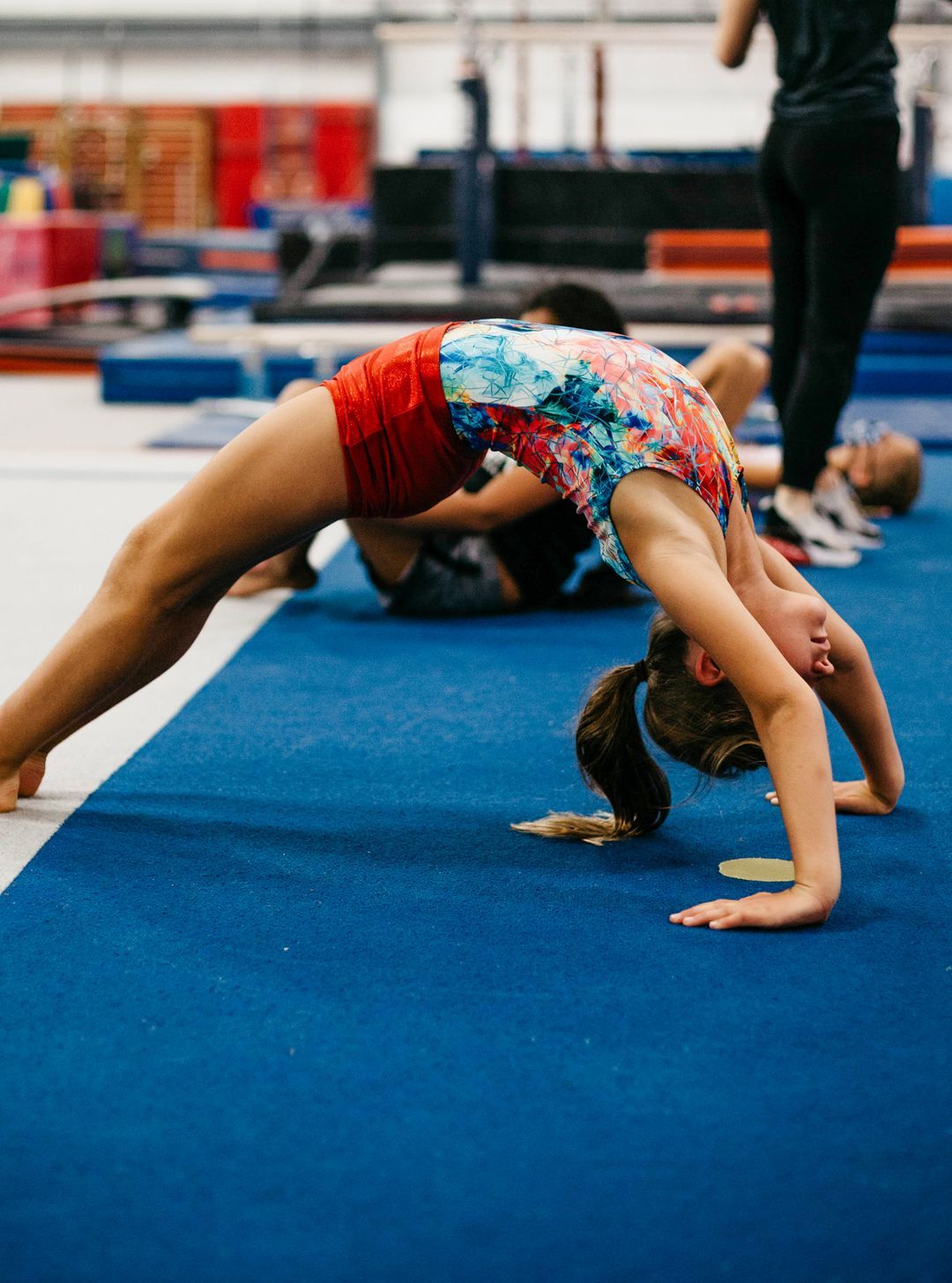 A young girl is doing a handstand on a blue mat in a gym.