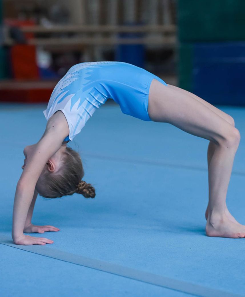 A young girl in a blue leotard is doing a handstand on a blue mat.