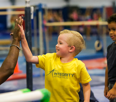 A young boy wearing a yellow integrity athletics shirt gives a high five