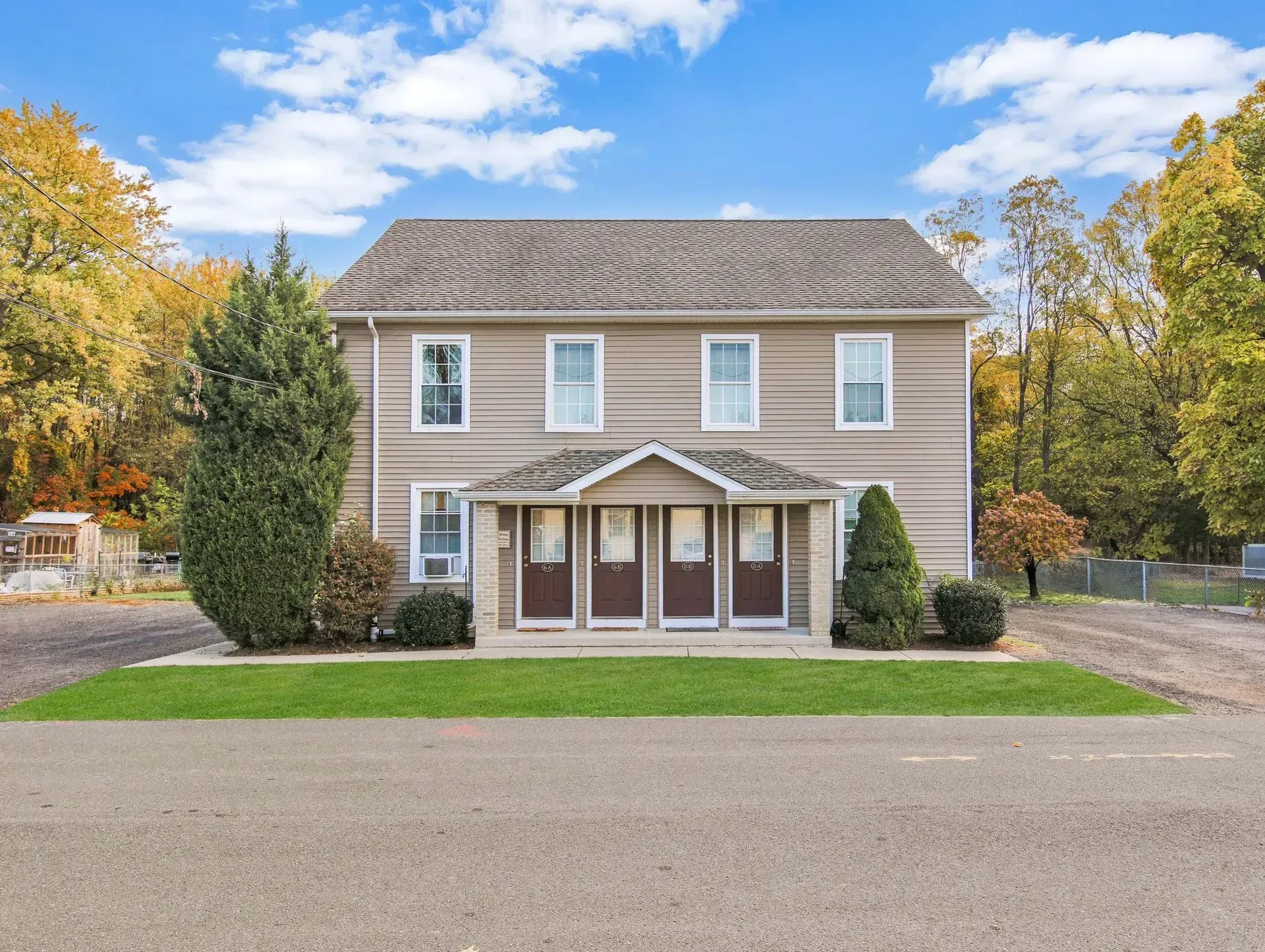 Two-story beige house with a front porch, green lawn, and trees in autumn