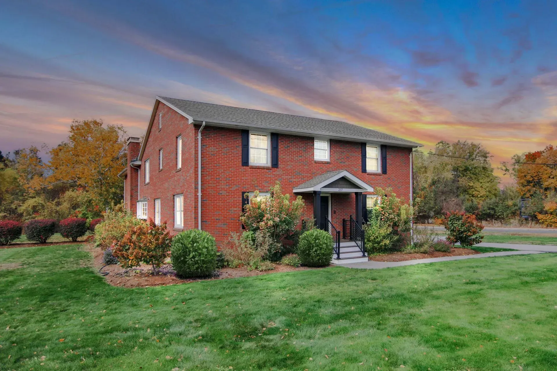 Two-story red brick house with a front porch and manicured lawn at sunset