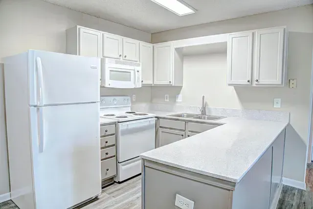 Bright white kitchen with cabinets, stove, microwave, refrigerator, and a peninsula counter