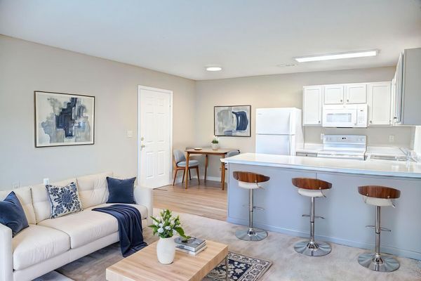 Bright open-concept living room with white kitchen, blue accents, and bar stools at a breakfast counter