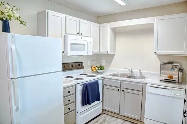 Bright white kitchen with stove, refrigerator, sink, microwave, and cabinets; blue towel on oven handle