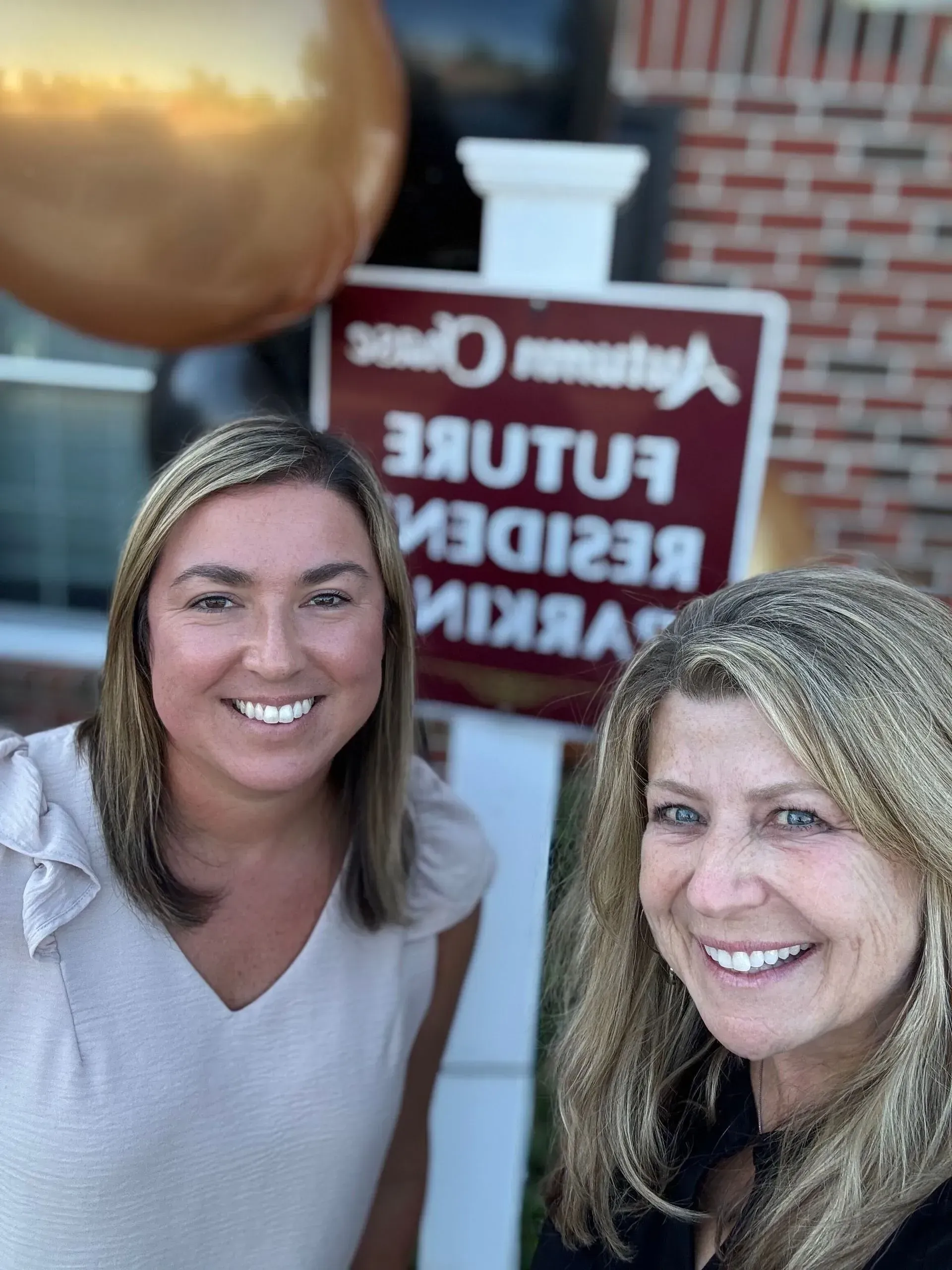 Two smiling women posing in front of a “Future Resident Parking” sign.