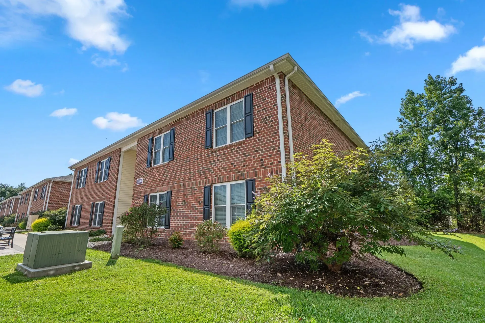 Brick apartment building with white shutters, green lawn, and blue sky on a sunny day