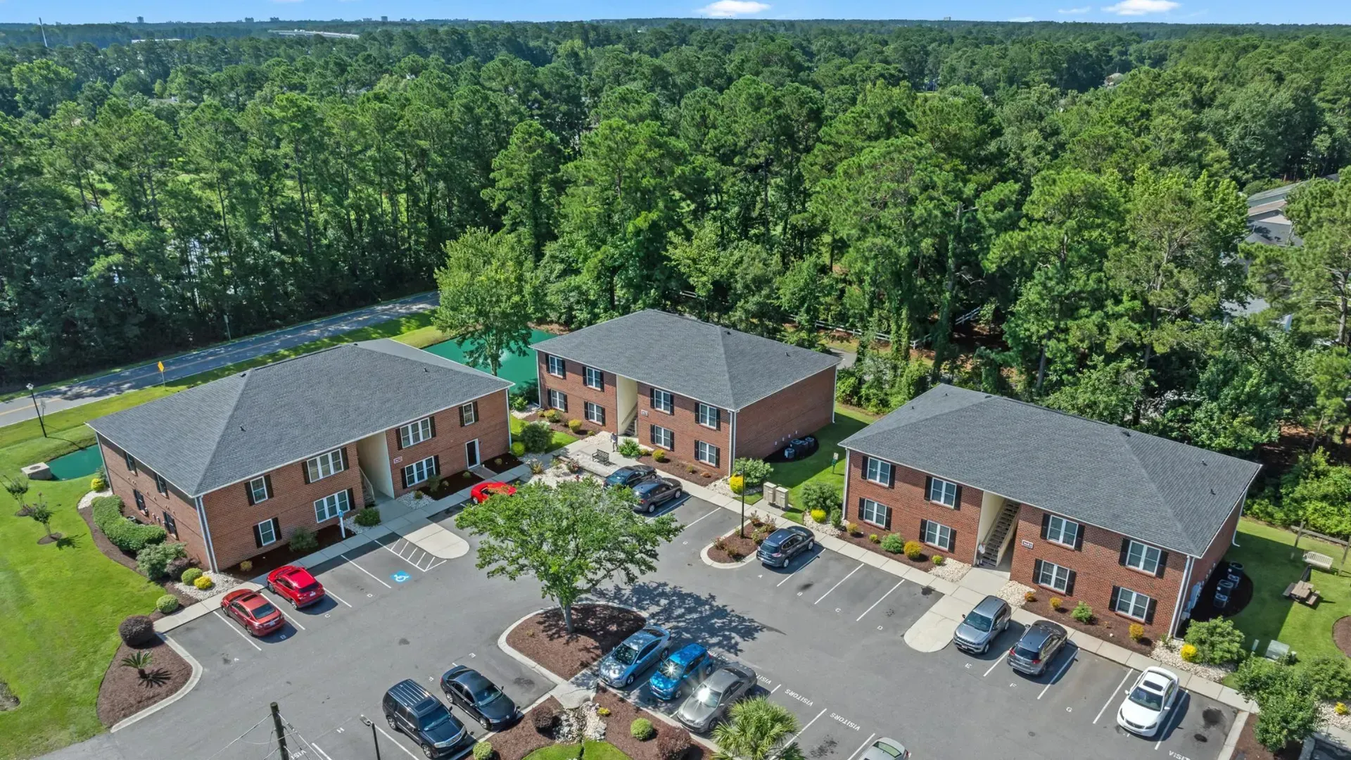 Aerial view of a brick office complex with parking lot, surrounded by dense green trees.