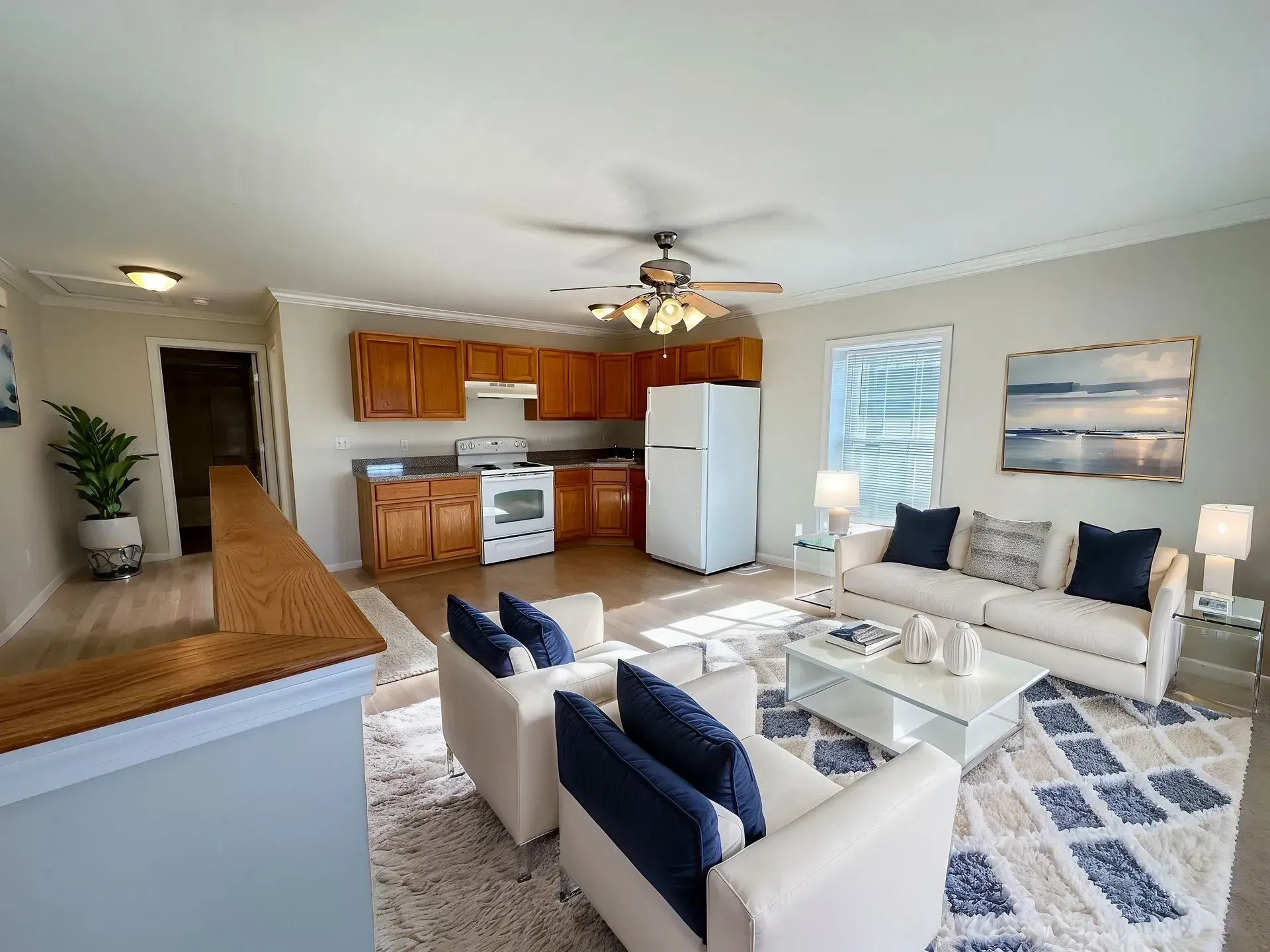 Bright open living room and kitchen with white sofas, blue accents, wood floor, and ceiling fan
